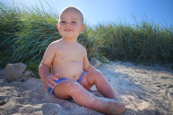 Neşeli küçük bir çocuk sıcak deniz kumlarında oynar ve dinlenmekten zevk alır.