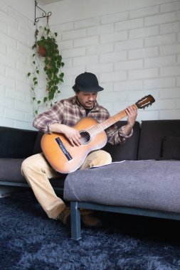Evde oturup gitar çalan bir adam.
