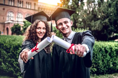 Ailelerimiz bizimle gurur. Mutlu mezunları üniversitede çerçevesi içinde açık el gülümseyen ve kameraya bakarak diploma ile ayakta.