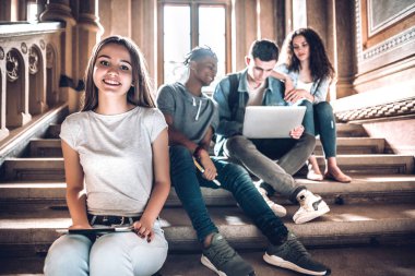 Üniversite hayatı. Güzel bir genç öğrenci arkadaşları ile dizüstü bilgisayar çalışırken tableti kullanarak kampüs merdivenlerde oturan.