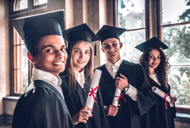 Gurur mezunu olmak. Kameraya bakarak gülen ve birlikte üniversitede ayakta grup gülümseyen Koleji mezunları.
