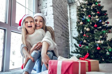 Anne ve kızı kırmızı Noel şapka yakınındaki bir Noel ağacı olarak portresi. Alt görünümü