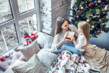 Hediye kutusu gülümseyerek ve gönderme anneme mevcut tutan kız. Mutlu çocuk kız Noel hediyesi ile Noel ağacı yakınındaki Satılık alışveriş satın aldı. xmas tatil gönderen hediye. üstten görünüm