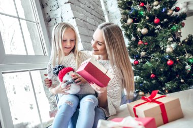 Mutlu Noeller ve mutlu tatiller! Neşeli anne ve sevimli kızı hediye alışverişi. Anne-baba ve küçük çocuk kapalı Noel ağacı yakınındaki eğleniyor.