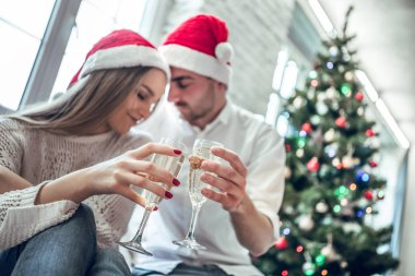 Yeni yıl. Noel. Seviyorum. Genç çift şampanya içiyor, birbirine bakarak ve gülümseyen Xmas ağacı evde yakın: