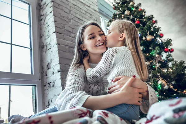 Happy Mom congratulates the child with a Happy New Year and Christmas in a decorated room for Christmas. kisses motherhood, childhood