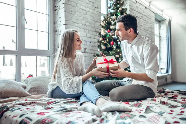 Güzel genç çift evde kutluyor. Yakışıklı adam kız arkadaşı bir hediye kutusu veriyor