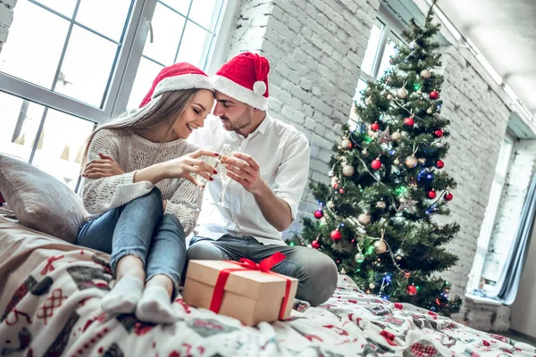 Noel Baba şapkaları güzel genç çift bardak şampanya tutarak ve süre evde yeni yıl kutlama gülümseyerek. Alt görünümü