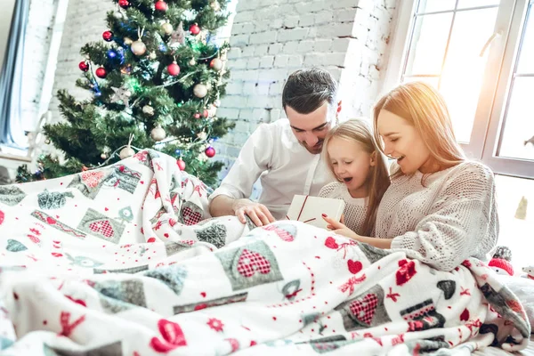 Family hugging near christmas tree on the bed. New year\'s morning. Cozy holiday at the fir-tree. love, happiness and family concept