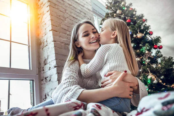 Happy Mom congratulates the child with a Happy New Year and Christmas in a decorated room for Christmas. kisses motherhood, childhood
