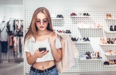 Alışveriş zamanı. Dükkanda duran ve smartphone kullanarak çanta ile genç kız.