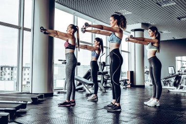 Grup içinde jimnastik salonu kas esneme dumbbells ile mutlu kadın. Fitness, spor, eğitim ve yaşam tarzı kavramı