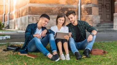 Grup çalışma oturumu. Çimde oturma ve ipad arayan öğrenciler kadeh.