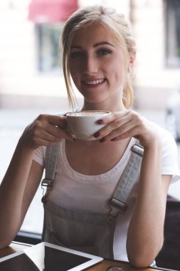 Büyük kahve bu gün daha da iyi yaptı. Onu sabah kafede kahve yudumlarken kameraya gülümseyen genç bir kadın.