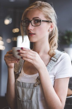Güzel bir gün zevk. Bir fincan tutarak ve kafede onun çalışma evinde otururken gülümseme ile kameraya bakıyor güzel genç kadın