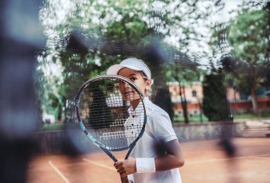Spor kulübünde tenis raketi olan küçük bir kız. Açık havada tenis oynayan küçük, sportif bir kızın görüntüsü. Tenis kortunda çocuk sporcu. Küçük çocuk için antrenman..