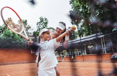 Tenis hocası ve tenis antrenmanındaki genç bir kız. Sahada çocuklara net olmayan bir şekilde hizmet etmeyi öğreten bir bayan tenis hocasının kırpılmış görüntüsü..