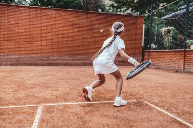 Küçük kız tenis topu vurmak öğrenme. Top ve raket kortu üzerinde küçük kız tenis oyuncusu. Çocuklar için aktif egzersiz. Arkadan görünüm