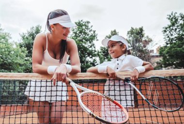 Mutlu aile içinde güzel beyaz spor giyim gülümseyen ve tenis kortunda tenis raketi tutarak portre.