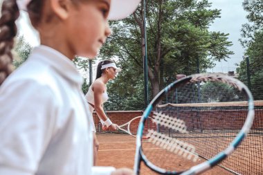 Küçük kızın hizmet bekliyor kapatın. Genç kadın ve küçük kızı sahada tenis oynamaya. Yan görünüm