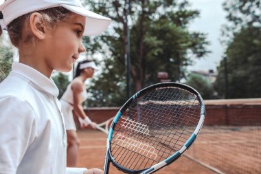 Kadın ve küçük kızı tenis kortunda tenis her iki dururken oynamaya. Yan görünüm