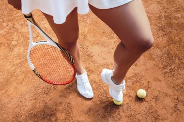 Oynamaya hazır mısın? Sportif genç kadın ayakları yere üstten görünüm kil tenis kortunda tenis topları ile kesilmiş. Seksi tenis oyuncu adımları inci spor kulübünde topa. Açık havada egzersiz.