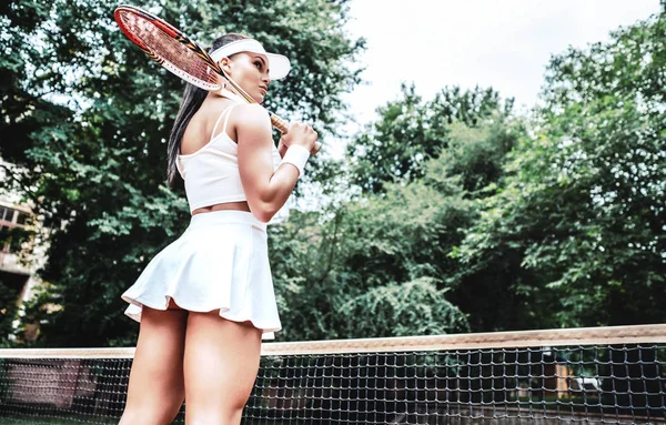 Girl holding racket. Sexy tennis girl. Female tennis player with racket. Healthy lifestyle concept. Of beautiful athletic girl in stylish sportswear holding racket in hand, to play tennis outdoors.