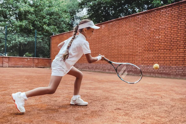 屋外のクレーコートでテニスの子 テニスコートで日焼けした少女の全身ショット 壁にテニス少女の子 子供のための夏の活動 — ストック写真