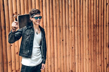 Kaykay ahşap arka plan ayakta omuzları üzerinde olan genç şık adam. Yaşam tarzı kavramı.