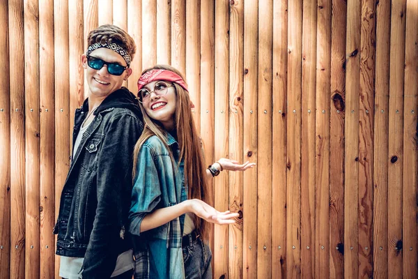 Stylish couple chatting when standing back to back near wooden background.Youth, lifestyle concept.