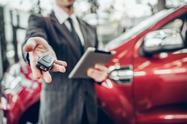 Gözlemci, arka planda bir araba ile bir araba anahtarı sunan takım elbiseli adam. Görünümü kapatın. Anahtar üzerinde odaklanmak