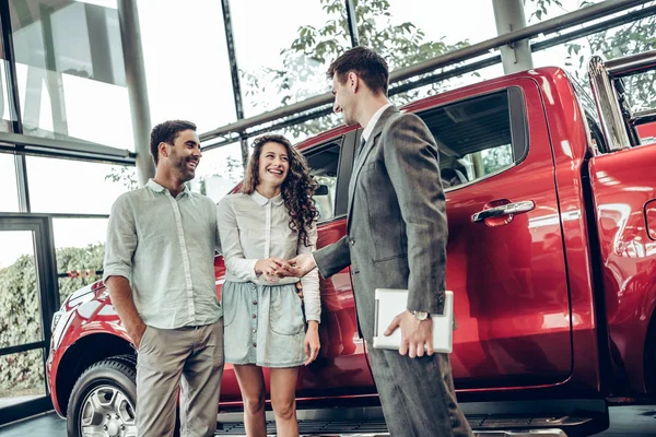 Now her dream comes true. Car salesman giving the key of the new car to the young attractive owners. Red car background