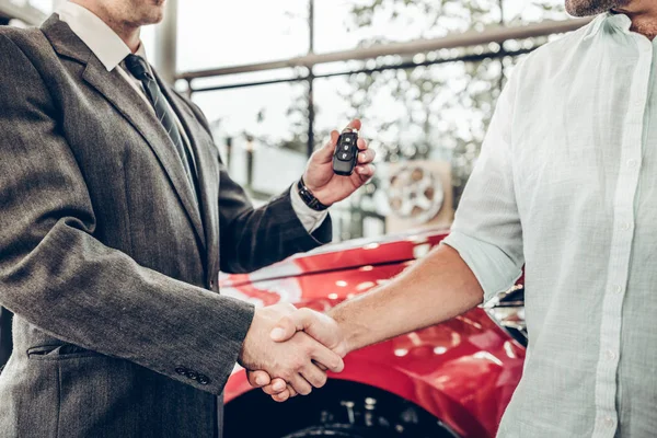 Auto business, car sale, deal, gesture and people concept - close up view of dealer giving key to new owner and shaking hands in auto show or salon