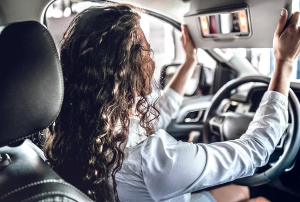 Young woman testing new car in salon. Woman looking on rearview mirror