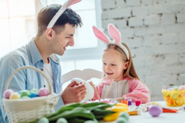 Babamla Paskalya için hazırlanıyor. Baba ve kızı birlikte küçük Paskalya tatili için hazırlarken iyi eğlenceler. Bir sepet Paskalya yumurta, çiçek ve boya tablodur.
