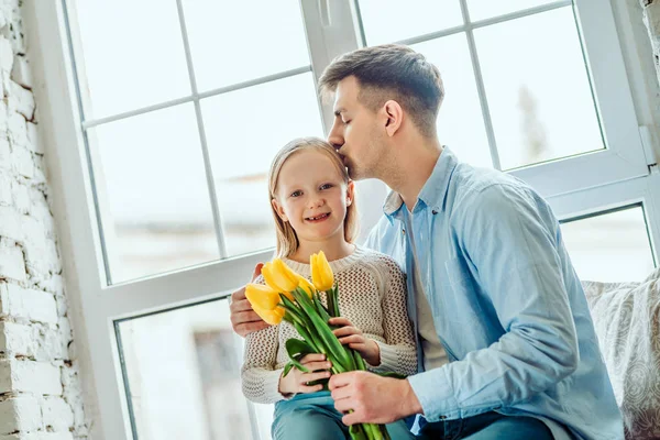 Every moment with her is precious. Daughter and father sitting together on the windowsill at home. Little kid holding bouquet of tulips. — Stock Photo, Image