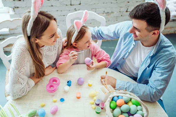 一緒にイースターの卵をペイントするので興味深いです。幸せな家族は、イースターの卵を一緒に描きます。平面図です。復活祭の卵を押しながら父と話す少女. — ストック写真