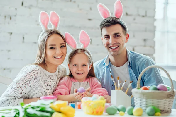 Pink rabbit ears add a festive atmosphere.Happy family paint easter eggs together.Little girl holding easter egg in hands.