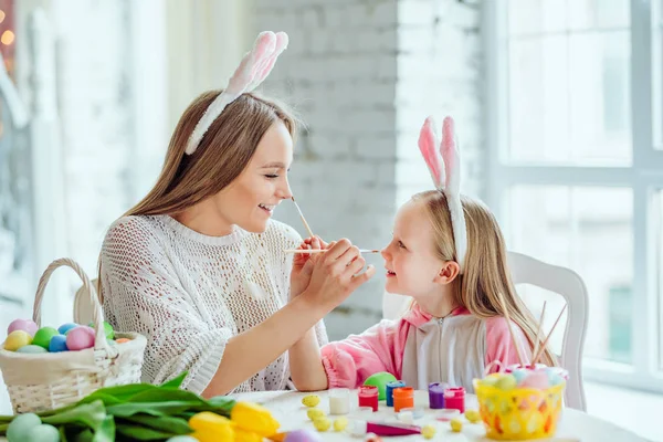 Frohe Ostervorbereitungen. Mutter und Tochter bereiten sich auf Ostern vor. Auf dem Tisch liegt ein Korb mit Ostereiern, Blumen und Farbe. — Stockfoto