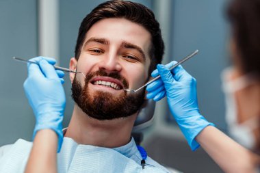 Klinikte diş aletleri tutan diş hekimi ile gülümseyen genç adam portresi. Görünümü kapat.