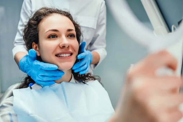 Una donna è seduta al ricevimento di un dentista. Si guarda allo specchio i denti. Un dentista è seduto uno accanto all'altro. Una donna sorridente. Felice concetto di paziente e dentista . — Foto Stock