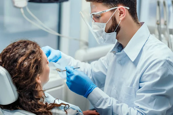 Dentiste très soigneusement vérifier et réparer la dent de sa jeune patiente. Vue latérale . — Photo