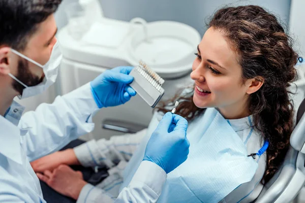Närbild porträtt av charmig ung kvinna sitter i tand stolen medan tandläkare välja färgtonen i tänderna. — Stockfoto