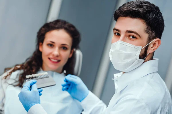 Dentist checking and selecting color of young woman\'s teeth looking at the camera close up view. selective focus.