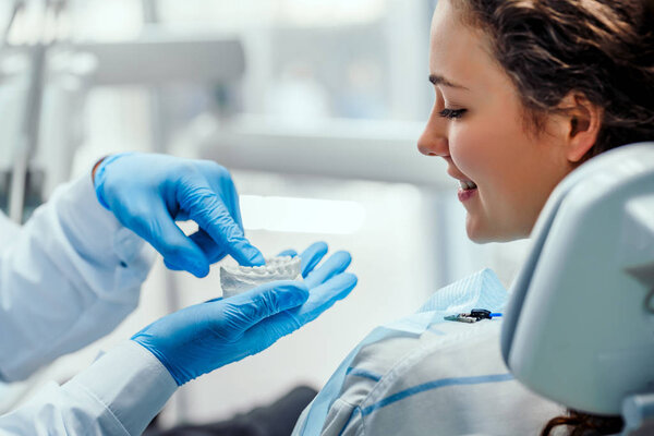 Male dentist showing his female patient how to brush teeth correctly, using dental mold. Mature woman watching her dentist explaining about teeth and gums care. Dentistry, perfect teeth concept.