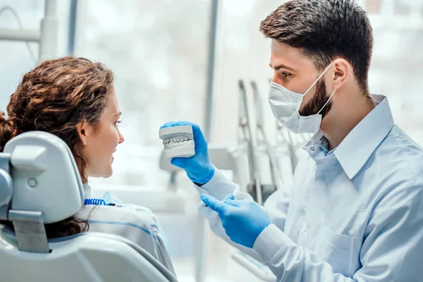 Dentysta rozmawia ze swoim pacjentem, pokazując jej dentystyczne formy. Widok z boku. — Zdjęcie stockowe