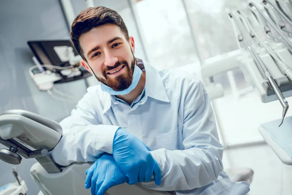 Dentiste souriant à la caméra à côté de la chaise à la clinique dentaire. — Photo