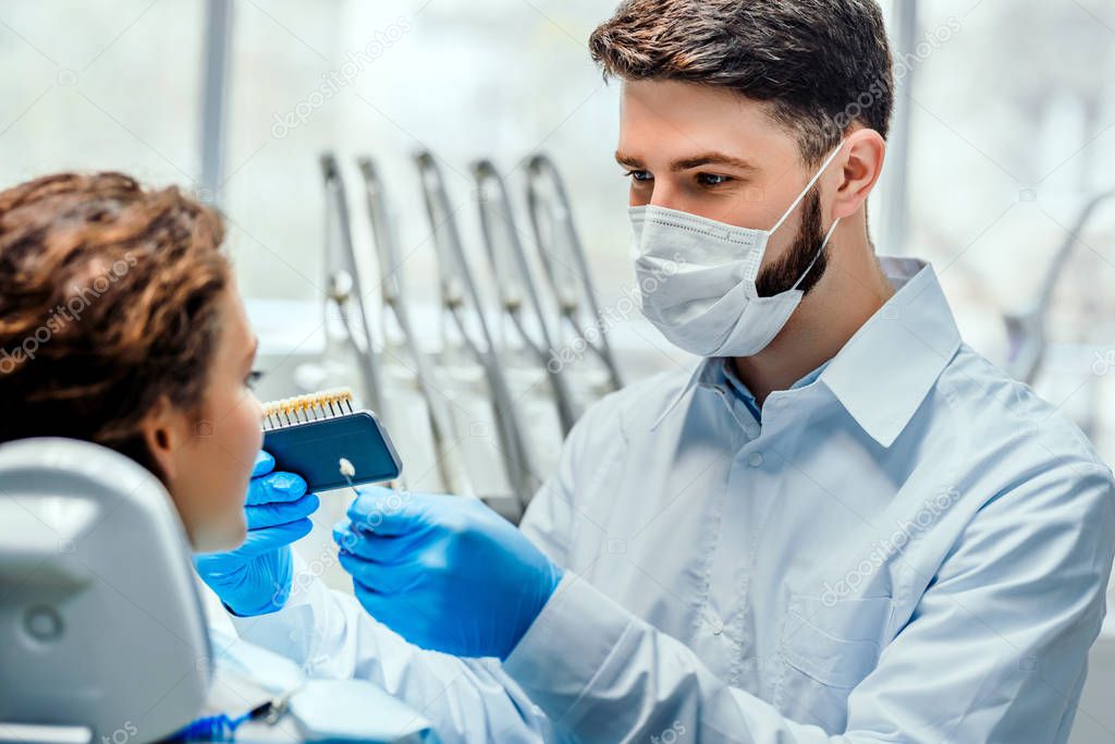 Dentist selecting patient's teeth color with palette in clinic. Side view.