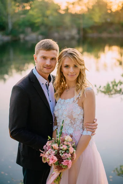 Retrato de casal recém-casado no fundo de um lago ao pôr do sol — Fotografia de Stock