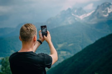 Genç adam akıllı telefon dağ zirveleri fotoğraf çekimi
